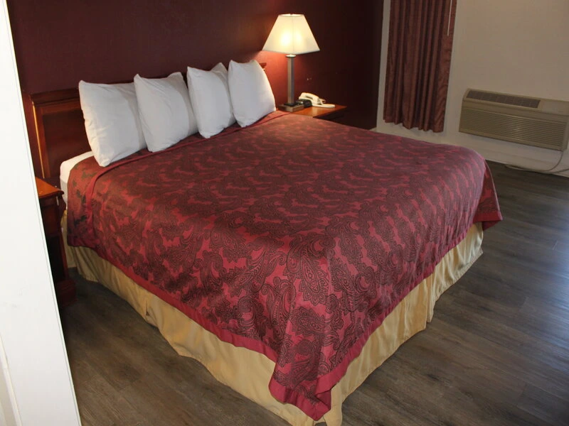 Hotel bedroom with king bed, burgundy comforter, white pillows.