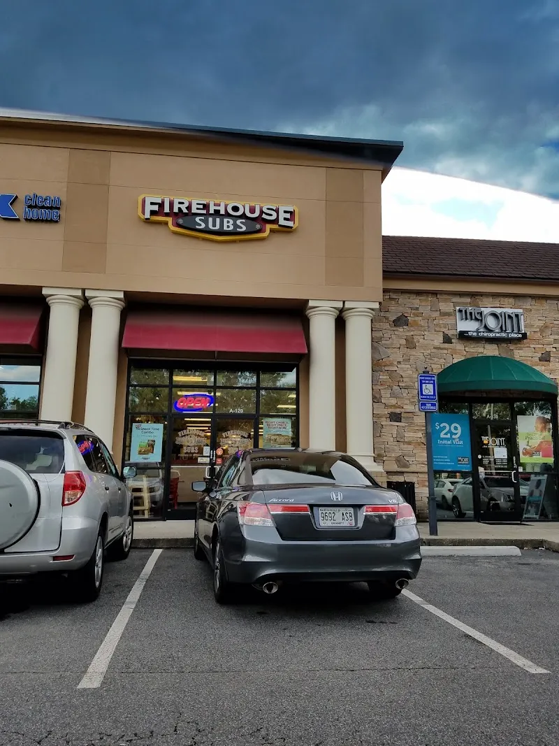 Firehouse Subs storefront in strip mall with parked cars and dark sky