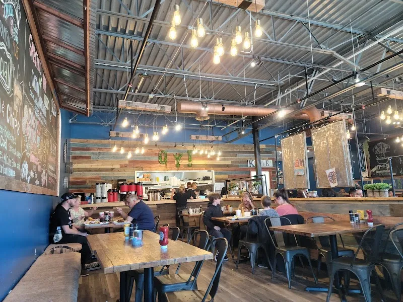 Rustic industrial restaurant interior with diners, Edison bulbs, reclaimed wood walls, chalkboard menu