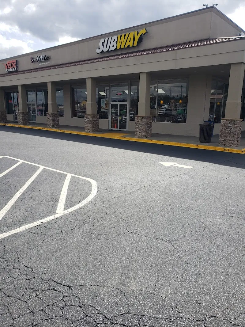 Subway restaurant storefront in strip mall with parking lot and cloudy sky