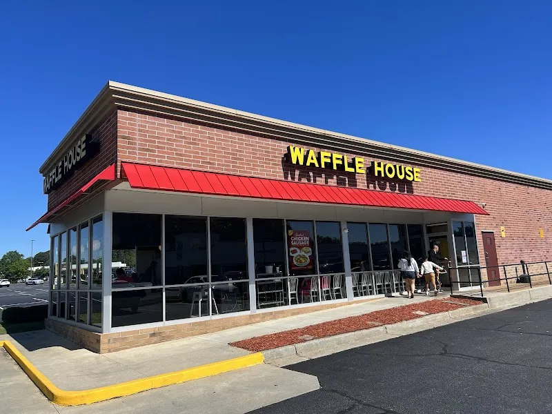 Exterior of brick Waffle House restaurant with red awning and customers entering.